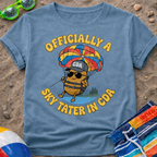Blue t-shirt with a humorous design of a potato skydiving, surrounded by beach items on sand.